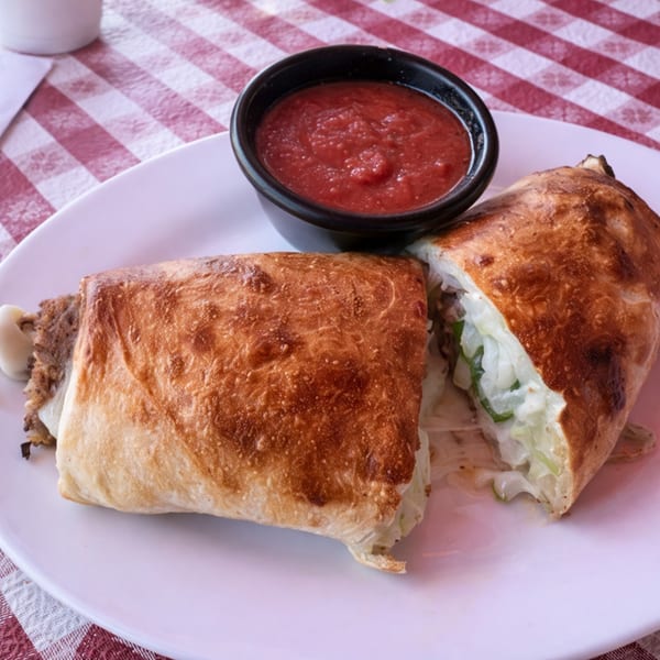 A calzone, cut in half to reveal its filling, served with a side of marinara sauce.