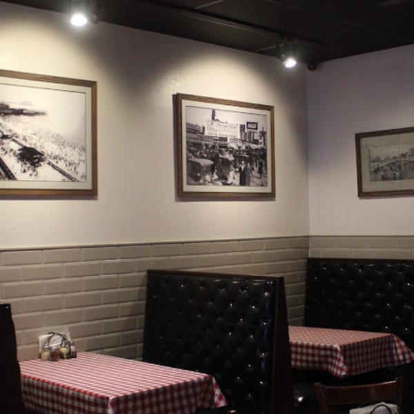 Restaurant interior with red and white checkered tablecloths, black booths, and framed historical photos on the walls.