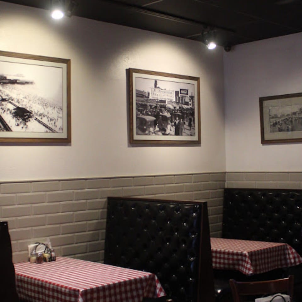 Restaurant interior with red and white checkered tablecloths, black booths, and framed historical photos on the walls.