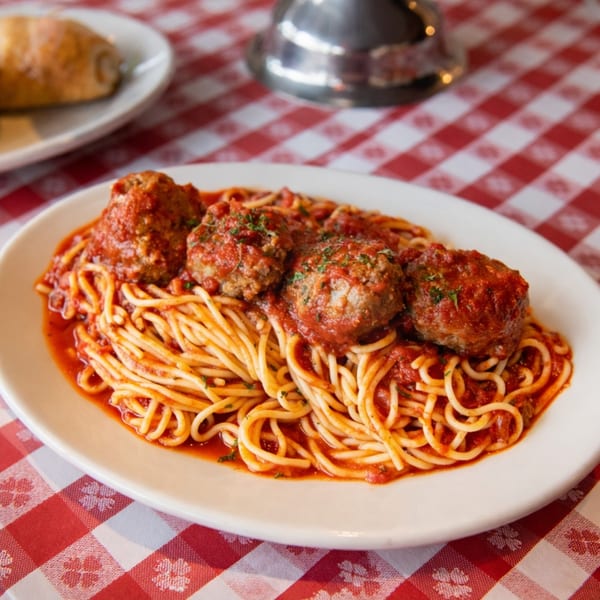 Spaghetti and meatballs with red sauce on a white plate, on a red and white checkered tablecloth.