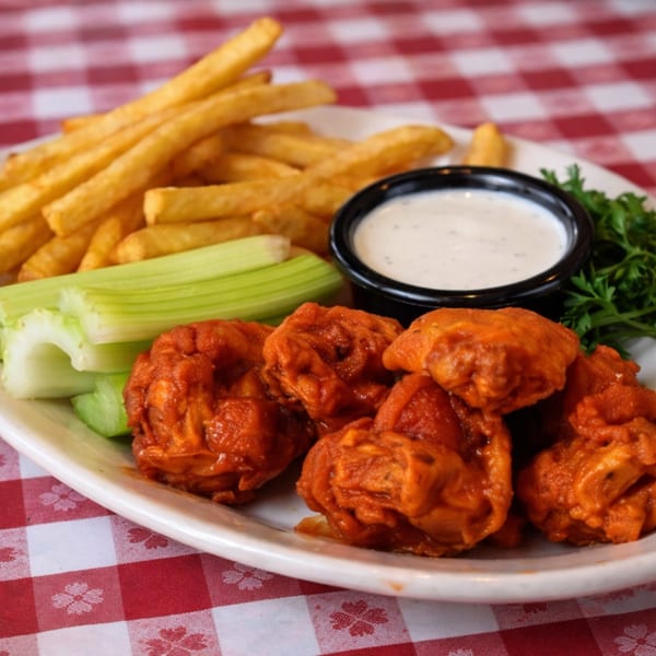Plate of buffalo wings, french fries, celery sticks, and ranch dressing on a red and white checkered tablecloth.
