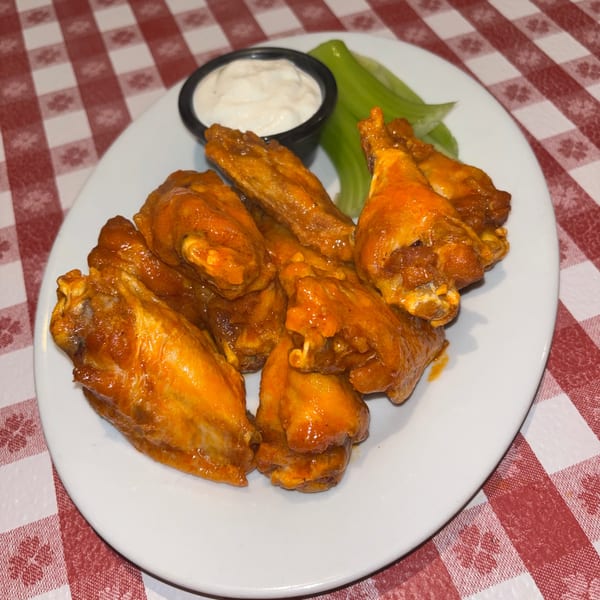 A plate of buffalo wings with ranch dressing and celery sticks on a red and white checkered tablecloth.